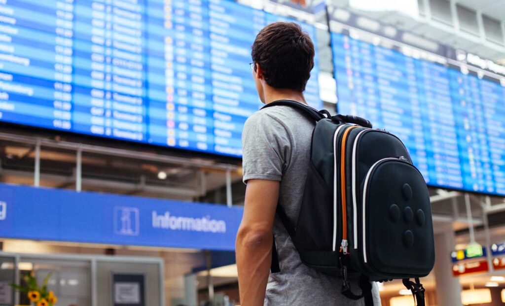 A man with his backpack looking at the the flight schedule of an airport