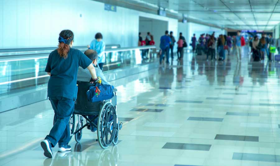 A caretaker pushing a wheelchair with an elderly on it on an airport