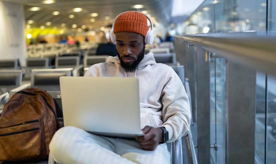 A man doing something on his laptop while wearing a headphones