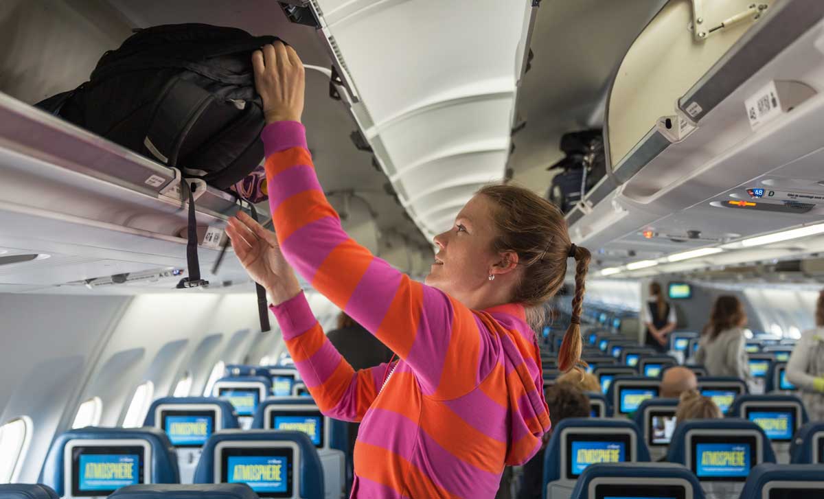 A woman putting her bag on the airplane compartment