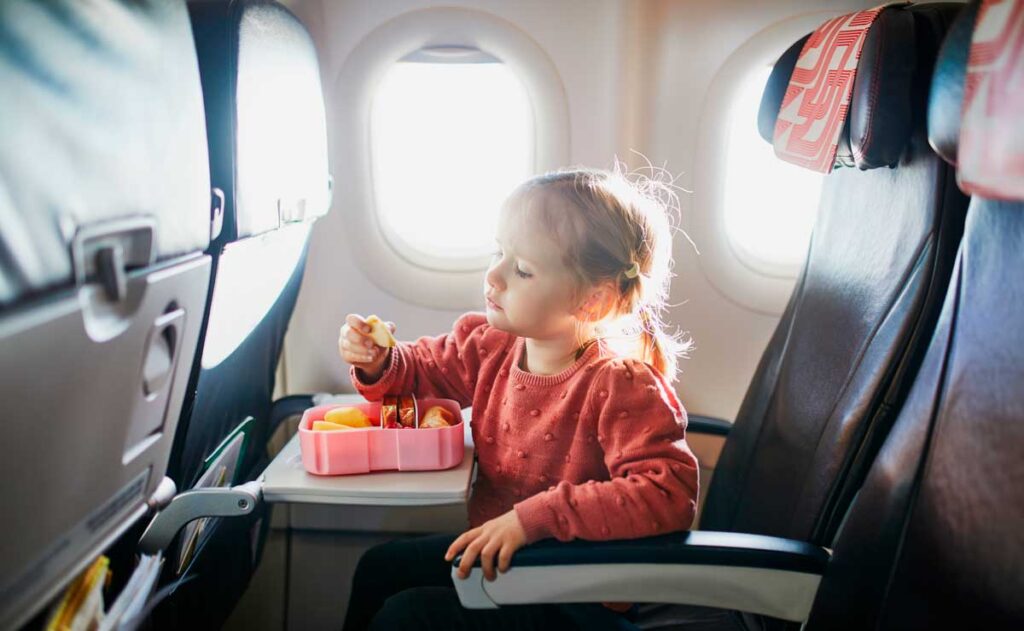 A toddler eating her food while on a plane