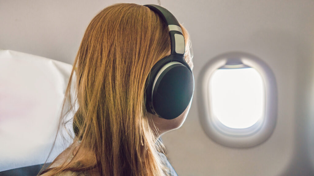 A woman wearing a bluetooth headphones while staring at the window on an airplane